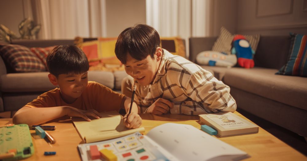 Evening Portrait of the Smart Young Boy Diligently Doing Homework Helpful Father Walks in the Living Room to Help with the Lesson.