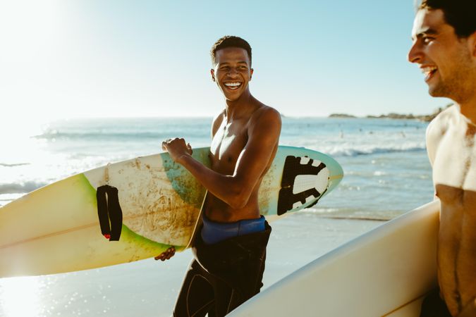 Smiling men walking on beach carrying surfboards