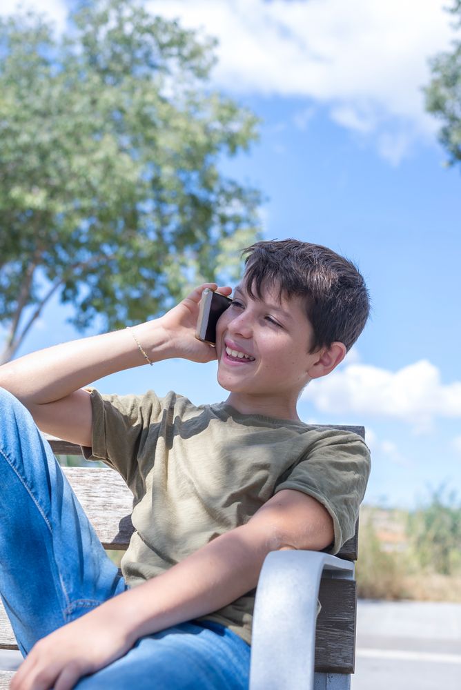 Teenager relaxing on bench speaking on cell phone