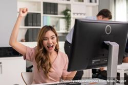 Asian woman with arm up in celebration while sitting at her desk 4Ndre0