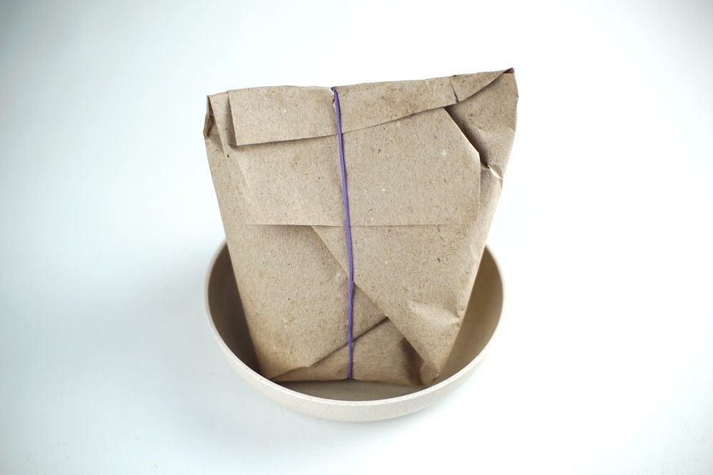 A brown paper wrapped rice bag in a bowl with a purple rubber band