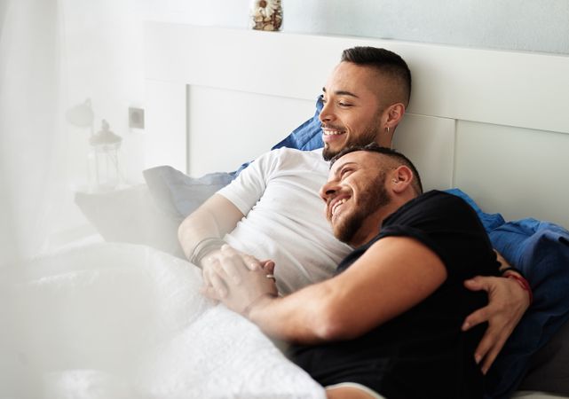 Smiling gay couple hugging on bed