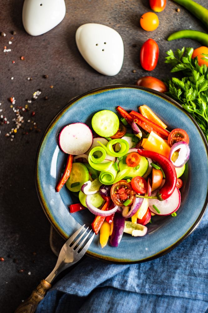 Top view of delicious healthy raw vegetable salad served on blue plate