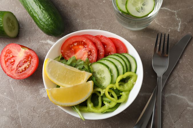 Plate with fresh vegetable slices and cutlery on grey background, close up