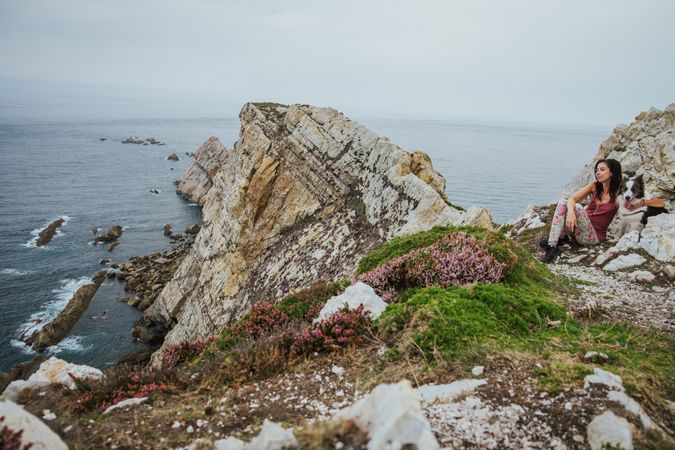 Adult tourist with dog on rocky coast on background of seascape in overcast