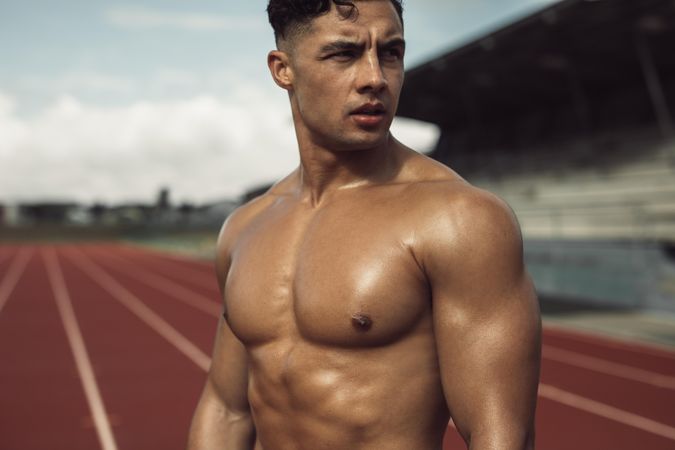 Athletic bodybuilder standing on track and field looking away