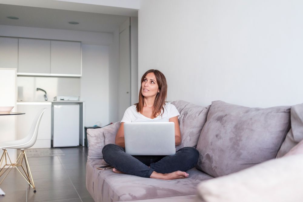 Smiling woman sitting on sofa working on her laptop in the morning