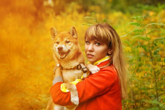 Female in red coat holding her cute shibu dog standing in field