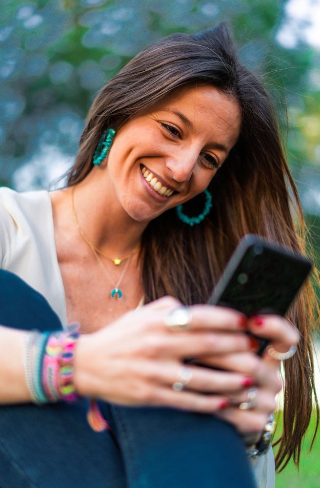 portrait of young woman using smartphone sitting on grass in park