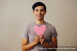 Romantic happy Hispanic male holding cut out pink heart to his chest 0PRJl4