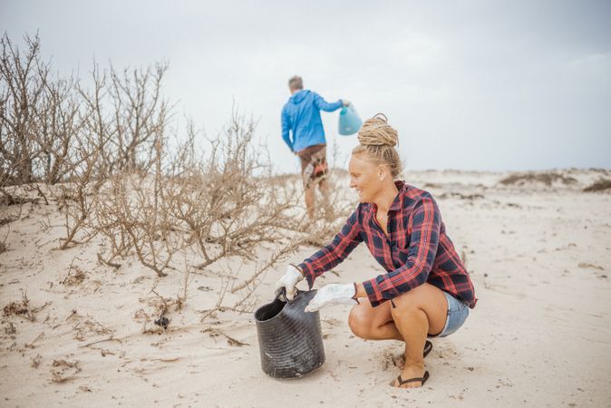 Content modern woman and man picking litter from sandy seashore