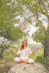 Happy woman practicing meditation on stone in forest
