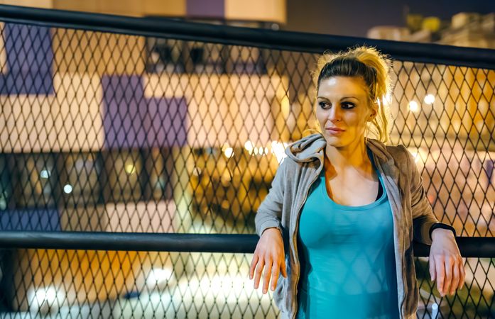 Portrait of woman wearing sportswear resting over banister at night in city setting