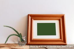 Rectangular wooden picture frame leaning against wall next to branch in glass mockup 5wNxR0