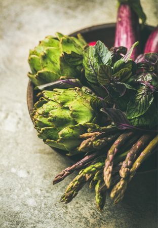 Green and purple vegetables on plate over grey background, selective focus