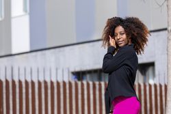 Black female putting her hair behind her ear while standing outside in the sun