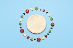 Raw pizza dough and vegetables on blue table