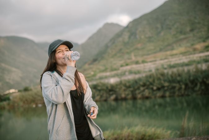 Woman drinking water near lake between mountains