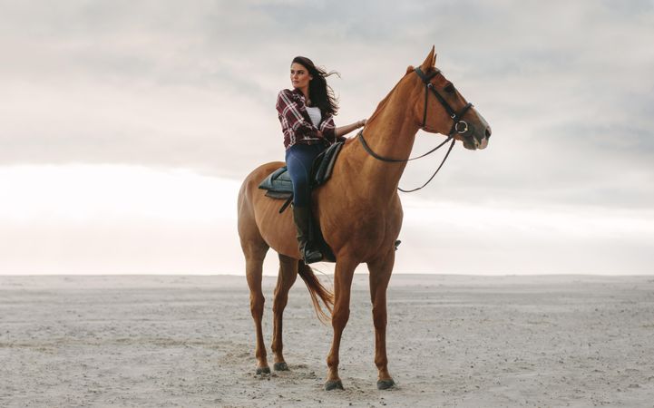 Full length of young woman on her horse at the beach with beautiful cloudy sky behind