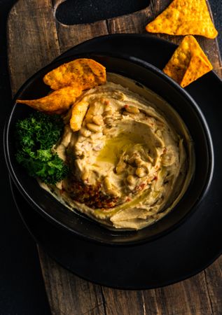 Looking down at creamy hummus dip in bowl with swirl of olive oil and chips