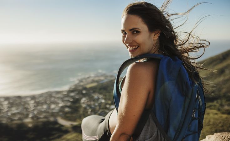 Happy female hiker sitting on top of a mountain and smiling over her shoulder