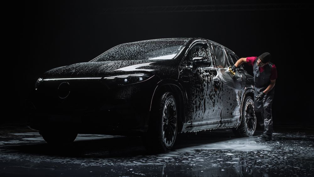 Portrait of an Adult Man Working in a Detailing Studio, Prepping a Factory Fresh Electric SUV for Maintenance Work and Car Care Treatment.