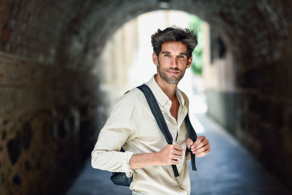 Portrait of dark haired man standing within arch of city street