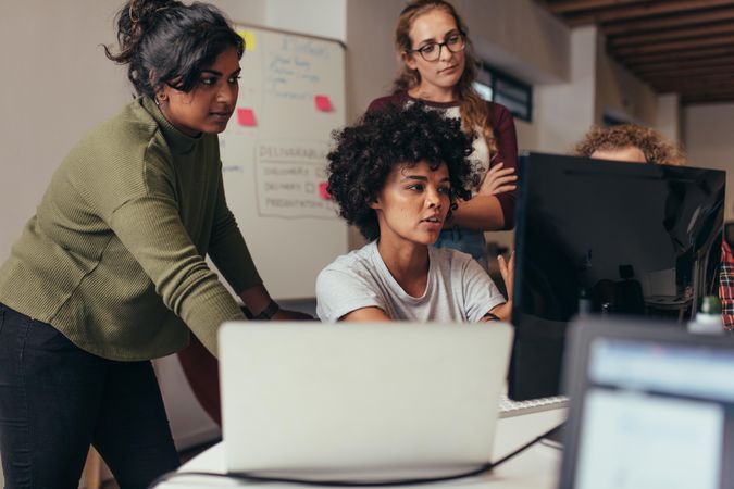 Woman programmer working on computer with colleagues standing by