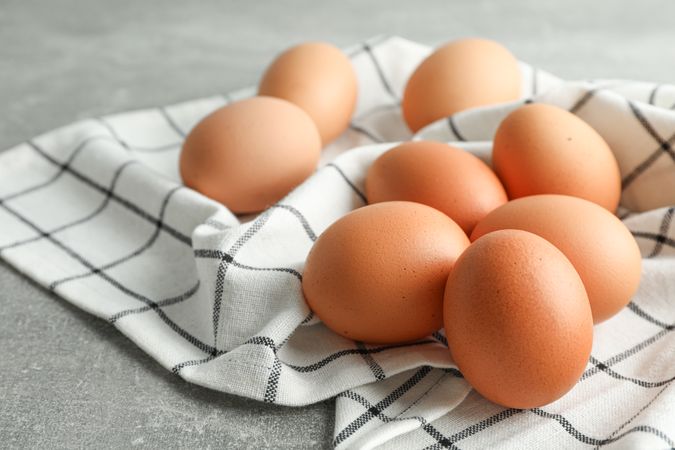 Brown chicken eggs in kitchen towel on grey background, space for text