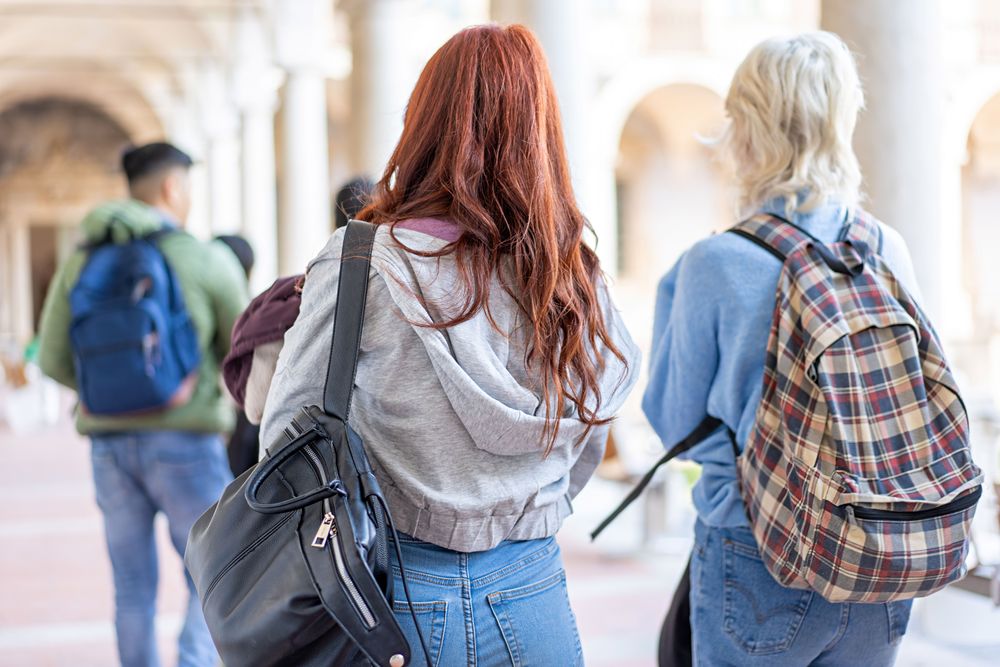 Back of diverse students with books and backpacks walking through campus
