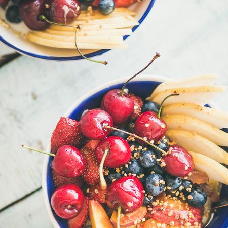 Two bowls of fresh fruit with cherries, peaches, blueberry, strawberries, square crop
