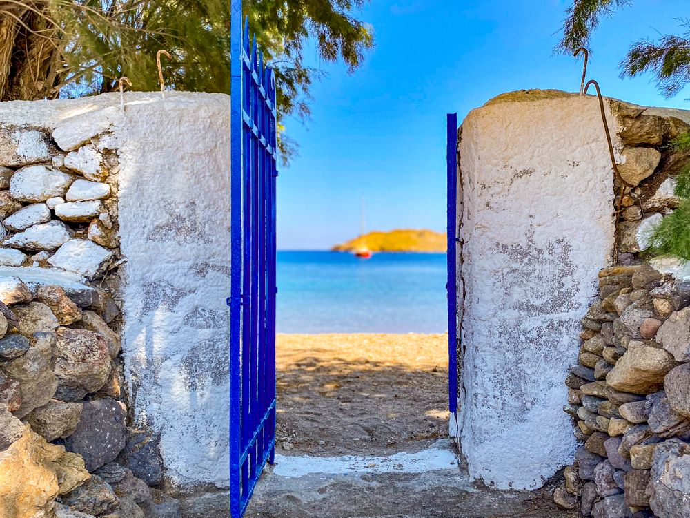 Open gateway to Meloi beach with view of docked red sailing boat