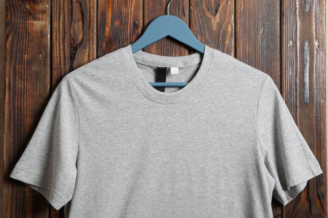 Hanger with blank gray t-shirt on wooden background, space for text