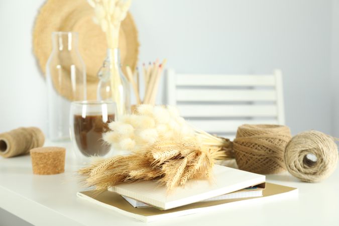 Table of arts and crafts supplies in bright home crafting room, with dried flowers, and notebook