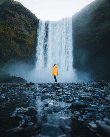 Person in yellow jacket standing near Skógafoss waterfall in Skógar, Iceland