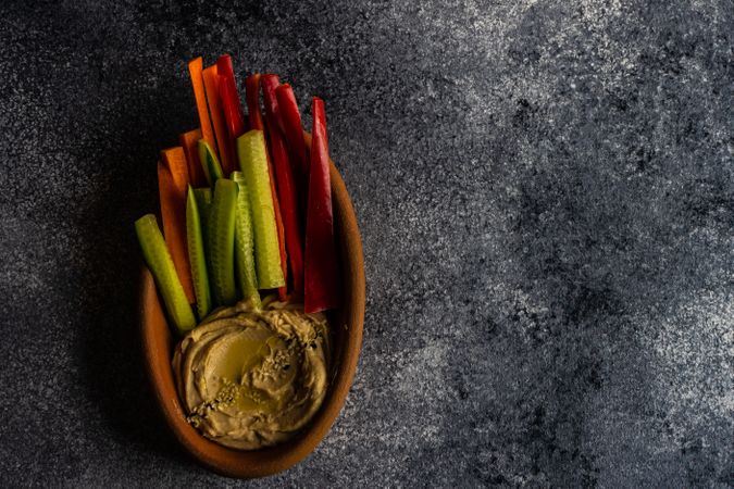 Top view of hummus dish served with chopped veggies on grey counter with copy space