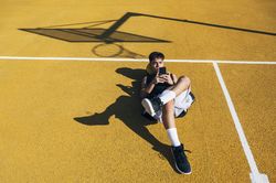 Male basketball player using his smartphone resting after training