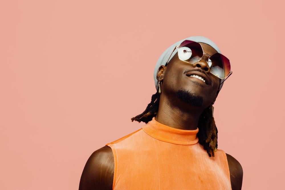 Portrait of a happy young man with sunglasses and cap laughing, isolated on pink