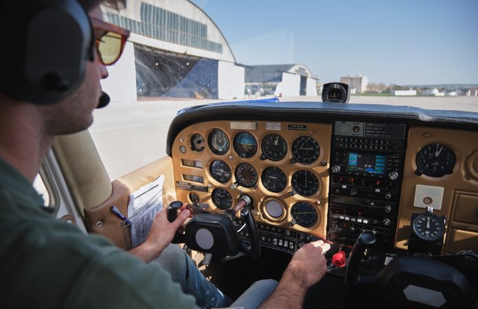 Young male pilot operating airplane parked on airfield on sunny