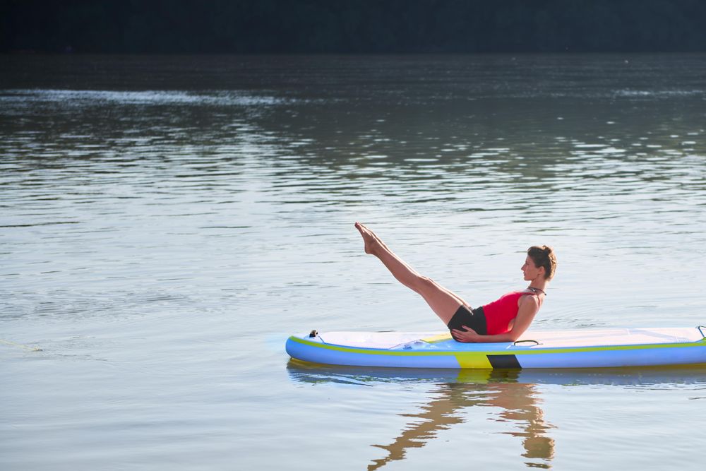 Woman doing ab workout on paddleboard in the sunrise