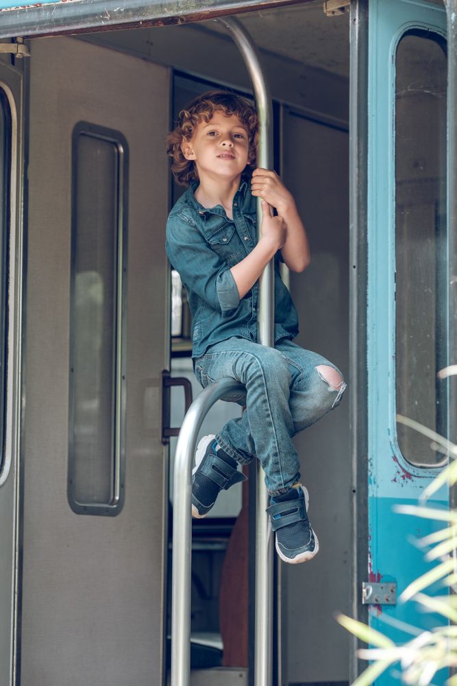 Preteen boy sitting on metal handrail of train