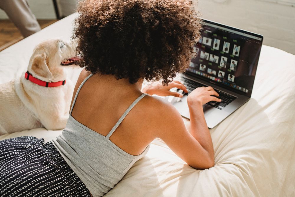 Woman laying on bed with a dog using laptop