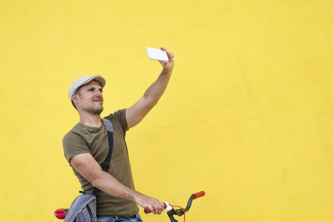 Male in hat and sunglasses taking selfie on phone while sitting on bicycle