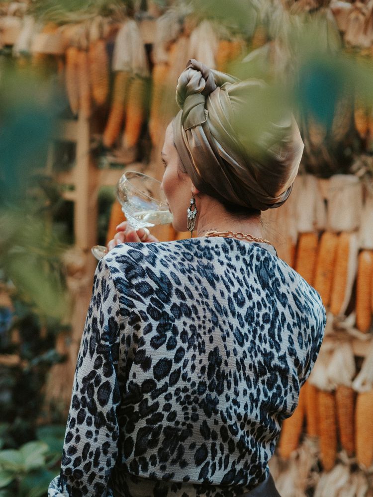Back view of woman in leopard shirt and green headwrap drinking a cocktail