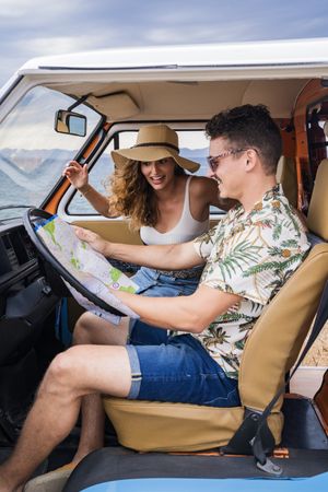 Touristic man exploring map with help of long haired woman in hat in front seat of car