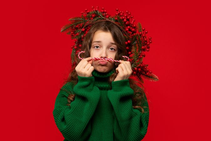 Girl making sad face while holding candy canes as mustache.