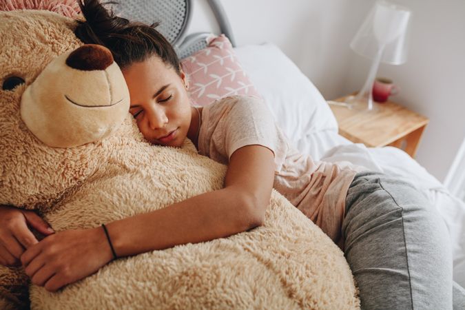 Girl sleeping on bed hugging a brown teddy bear