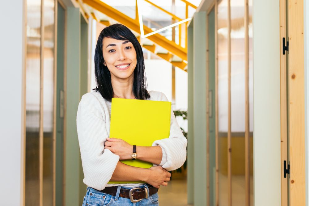 Portrait of smiling Asian woman looking at camera holding folder in modern office
