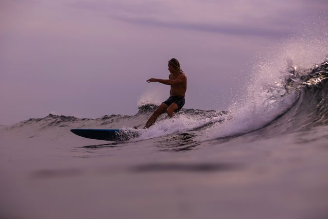 Man on surf board on waving water at sunset
