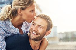 Woman kissing her boyfriend’s forehead on a sunny day